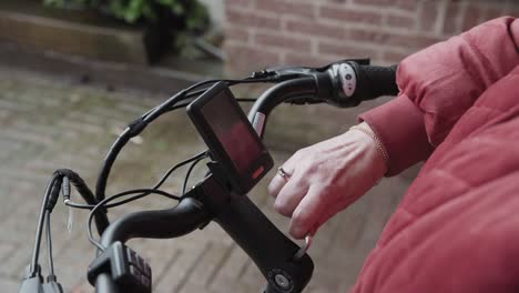 Lady-in-a-red-jacket-straddles-her-bike-as-she-is-tightening-the-handle-bar-adjustment-screws-on-a-E-bike-with-an-allan-key-outside