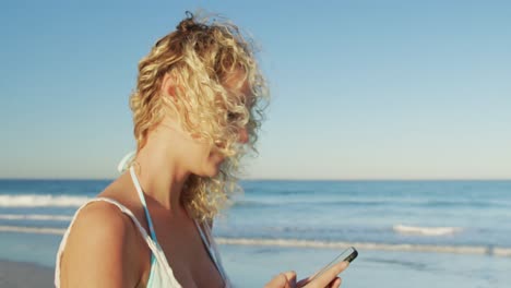 mujer joven usando un teléfono inteligente en la playa 4k
