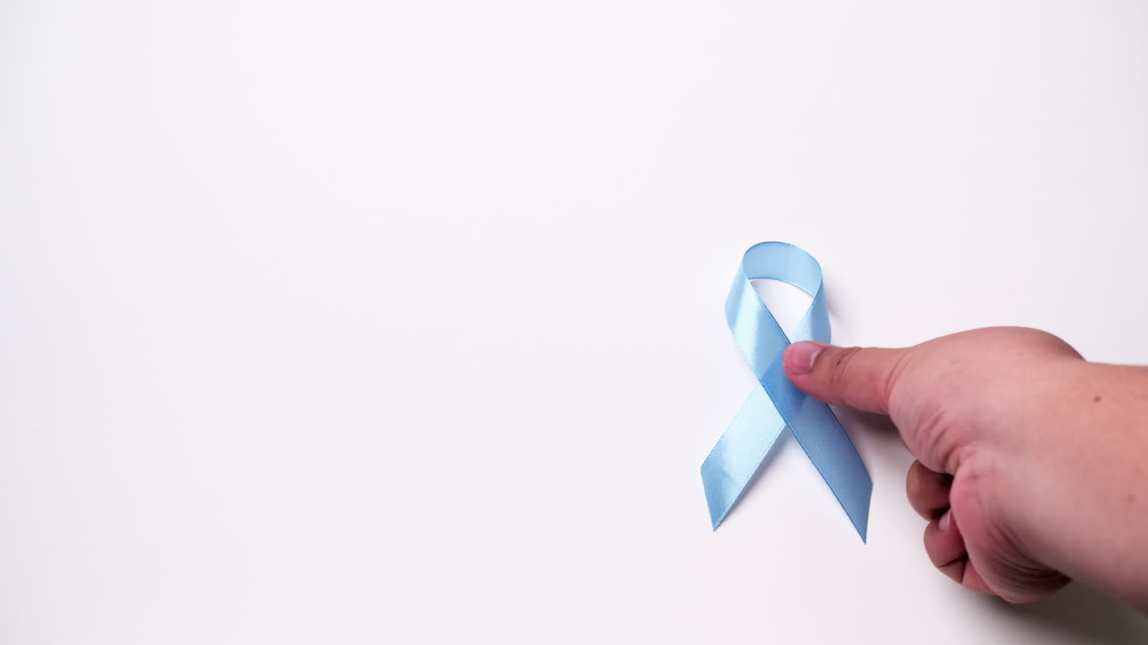 Dettaglio di mano maschile che posiziona un nastro di colore azzurro chiaro su sfondo bianco
