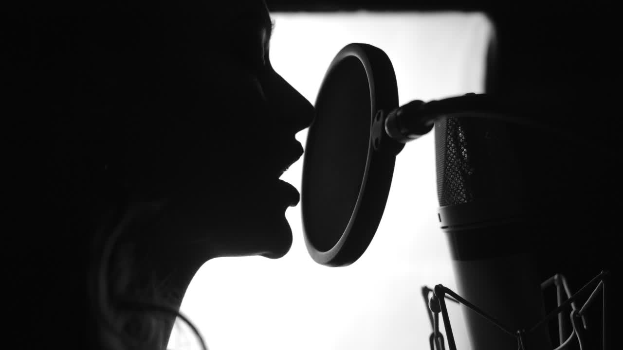 Side view of attractive female's face with perfect nose and pretty lips singing to the microphone. Singer standing in front of the mic and singing. Close-up. Black and white