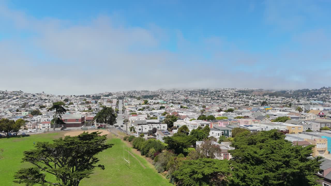 Drone descends over the Excelsior neighborhood in San Francisco, California, revealing colorful rooftops, residential streets, and hillside Bay Area urban scenery, ideal aerial city stock footage