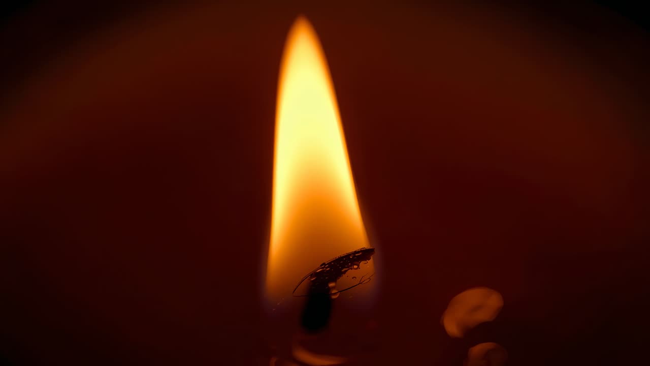 Subtle airflow causing candle wick flame pulsing, flickering, retracting over wax pool in dim room