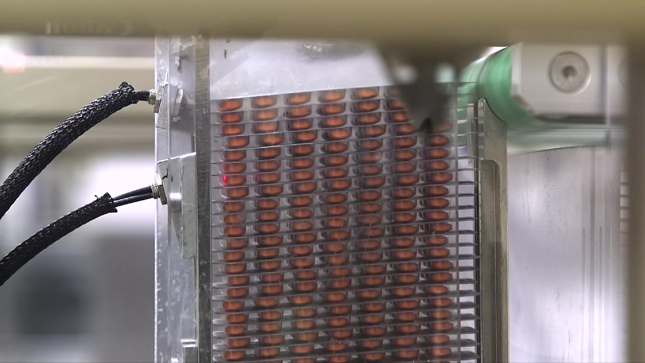 Close-up of filled pharmaceutical blister packs moving vertically through an automated packaging machine during tablet production in a modern manufacturing facility.