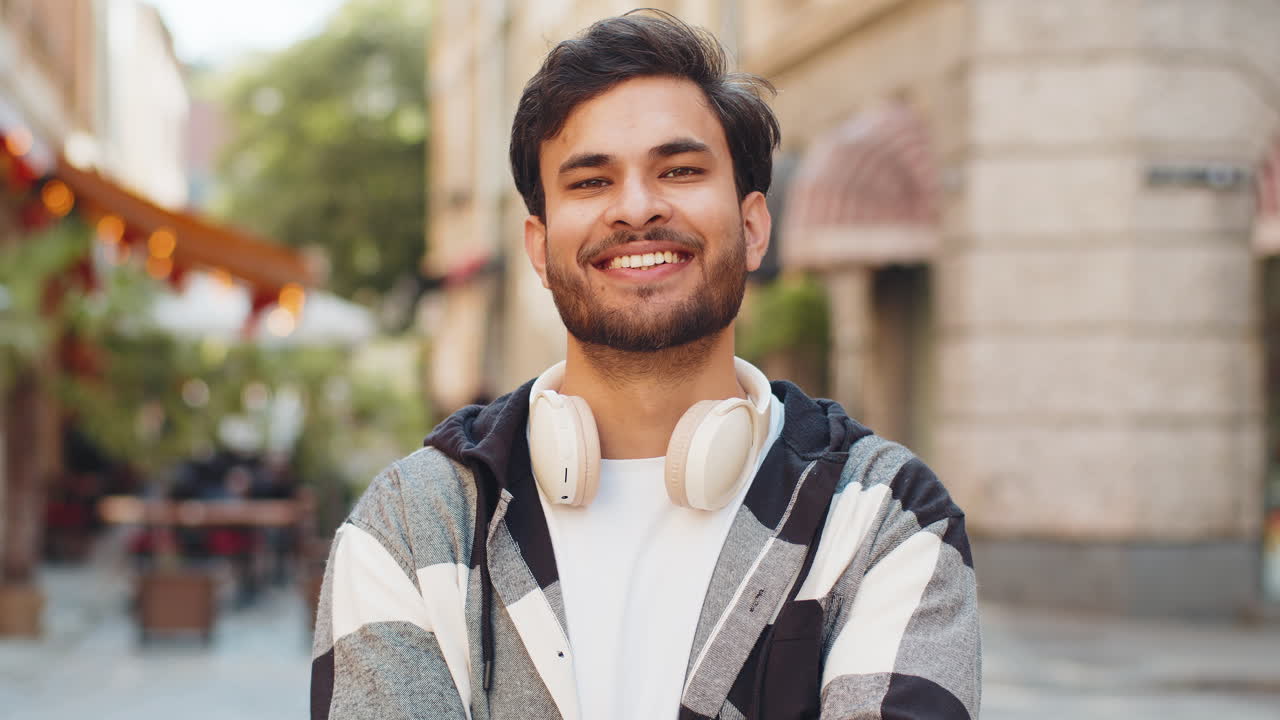 Smiling indian young man smiling at camera resting relaxation feel satisfied in city street