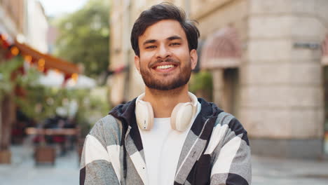 smiling indian young man smiling at camera resting relaxation feel satisfied in city street