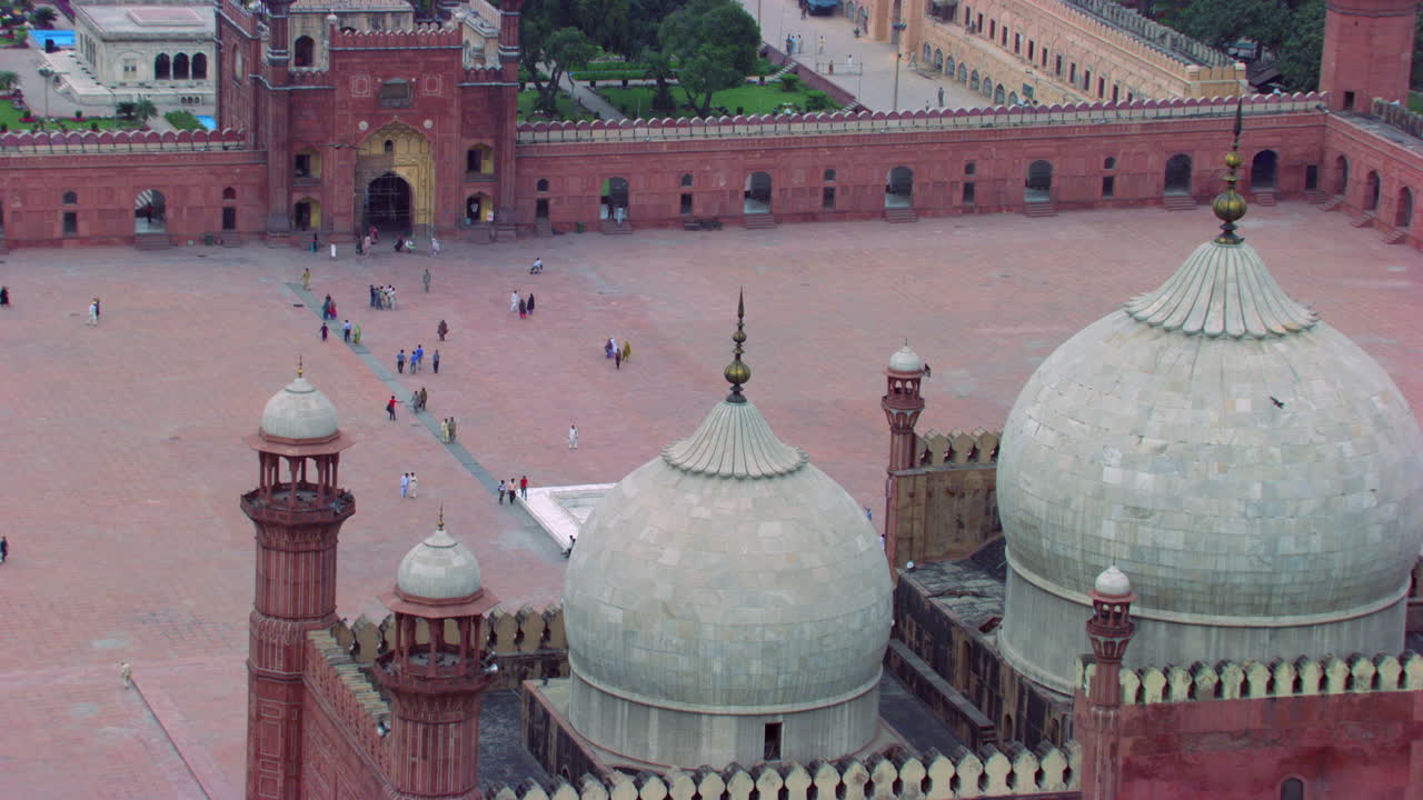 lahore, pakistán, vista de cerca del suelo y los minaretes de la mundialmente famosa mezquita badshahi, visitantes damas, caballeros y niños están en la mezquita, fieles en el suelo de la mezquita, cometas negras