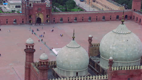 Lahore,-Pakistán,-Vista-De-Cerca-Del-Suelo-Y-Los-Minaretes-De-La-Mundialmente-Famosa-Mezquita-Badshahi,-Visitantes-Damas,-Caballeros-Y-Niños-Están-En-La-Mezquita,-Fieles-En-El-Suelo-De-La-Mezquita,-Cometas-Negras