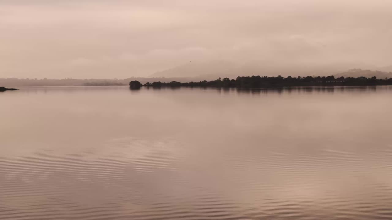 A serene sunset at Vaitarna Dam, where warm golden hues melt into gentle ripples across the calm waters, silhouetting distant hills and creating a peaceful, dreamlike evening landscape