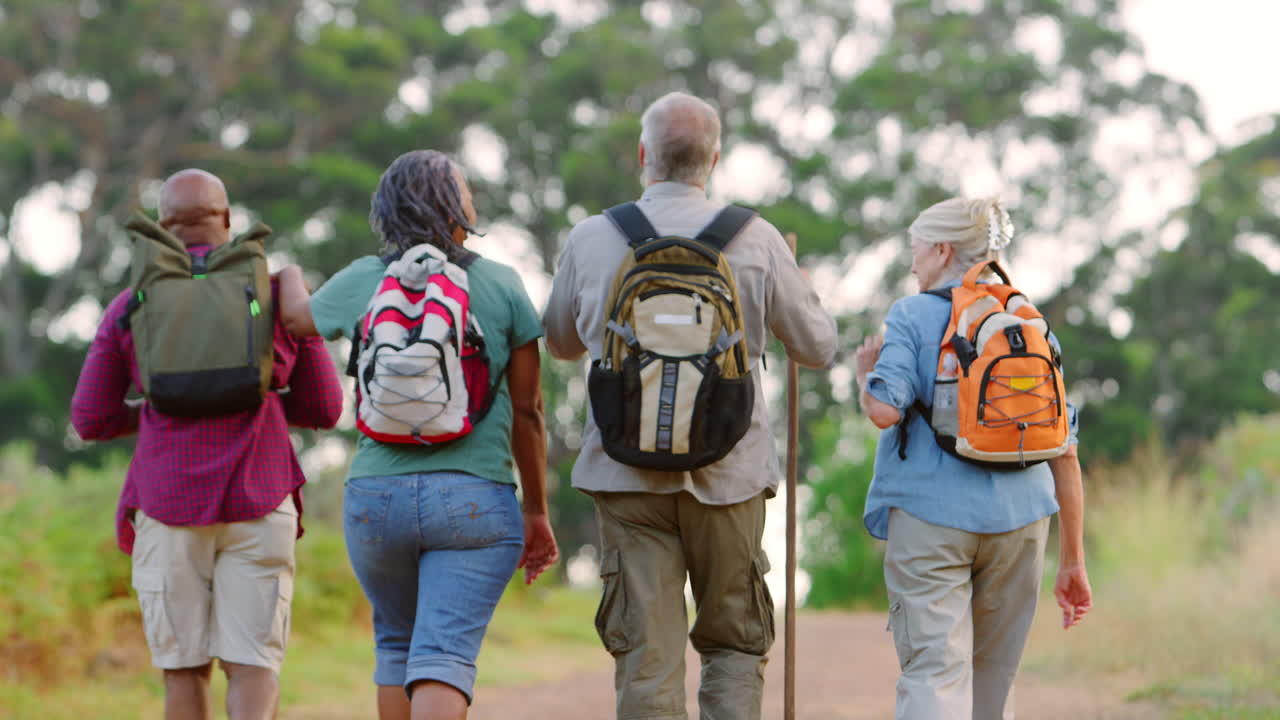 vista trasera de amigos mayores activos disfrutando de una caminata por el campo caminando a lo largo de la pista juntos