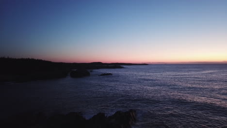 silhouette on man standing on rocky cliff and watching colorful lights before sunrise on ocean horizon