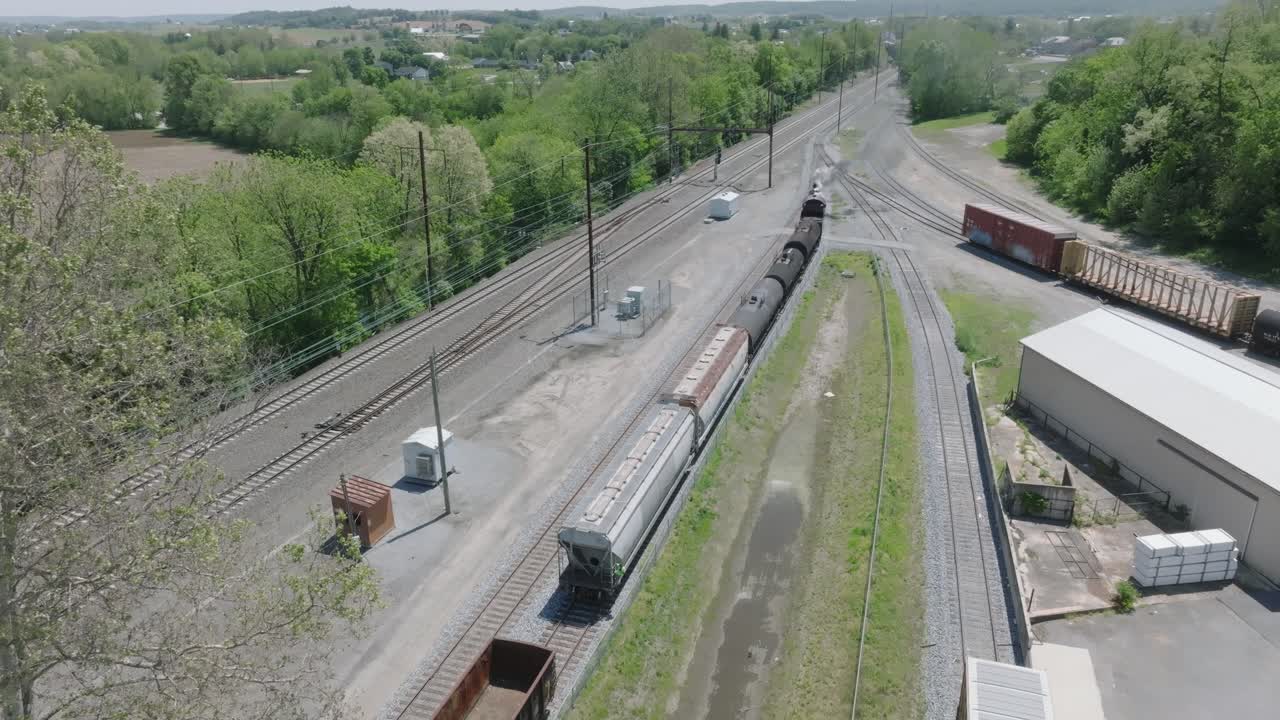 A vintage steam freight train makes its way backing up in yard performing switching operations moving steadily along the railway tracks in a peaceful countryside setting