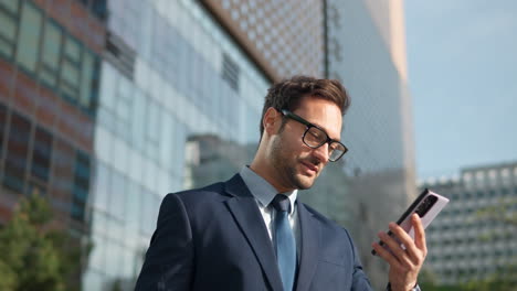 Cheerful-businessman-stand-in-the-city-center-street-talking-using-phone,-finish-conversation-smiling,-technology-communication-sunny-day-success-slow-motion