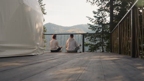 people meditate on glamping round house terrace at sunrise. woman and man enjoy early morning sitting in lotus poses together. relaxation practices for mind