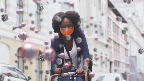 animation of covid 19 cells over african american woman in face mask using smartphone