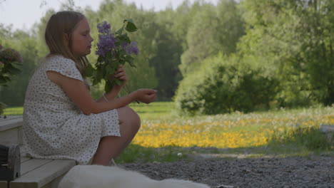 cute young girl with dog in idyllic nordic landscape, smelling summer flowers