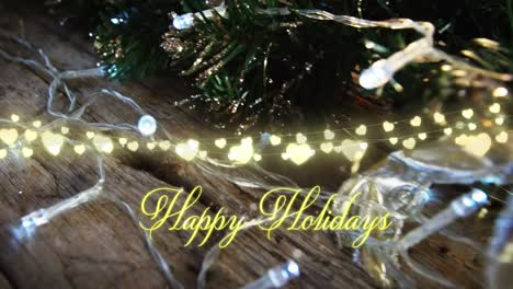 Animation-of-text,-happy-holidays,-in-yellow,-over-string-lights-and-decorated-christmas-tree