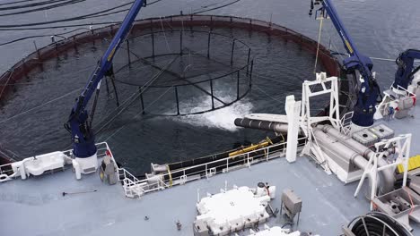 Static-drone-shot-of-a-well-boat-placing-fish-in-a-fish-cage-near-Uist