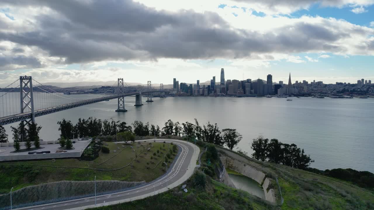A stunning horizontal drone shot ascending to reveal the iconic Bay Bridge from Yerba Buena Island, CA. Captures the bridge, water, and surrounding cityscape.