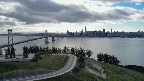 a stunning horizontal drone shot ascending to reveal the iconic bay bridge from yerba buena island, ca. captures the bridge, water, and surrounding cityscape.