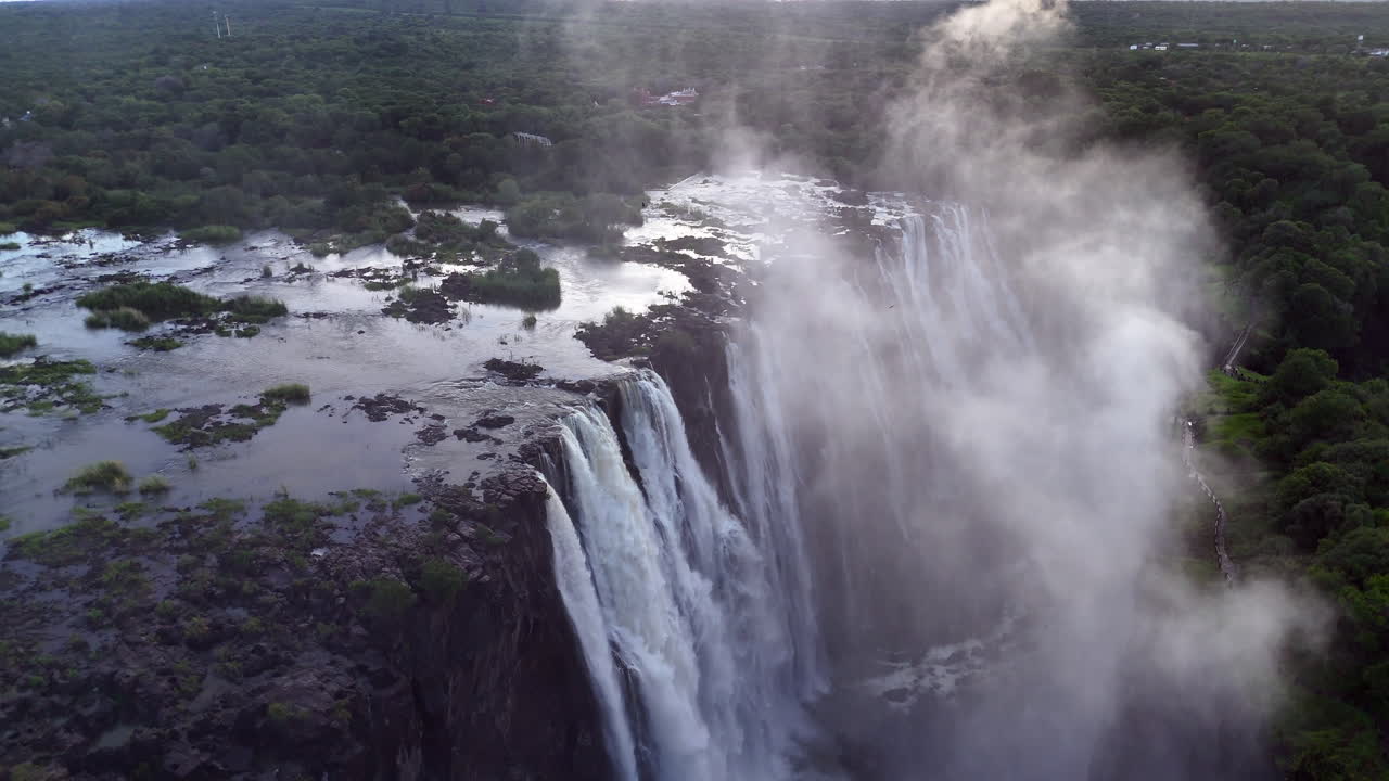 Aerial view of Victoria Falls with powerful waterfall plunging into gorge, mist rising above lush green forest, dramatic natural wonder and iconic travel destination in Africa