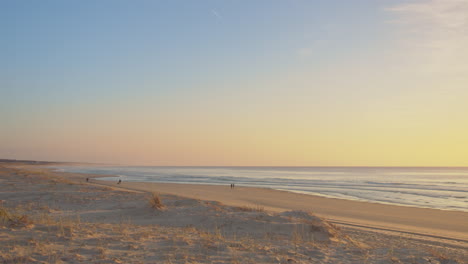 Peaceful-Sandy-Beach-At-Sunset-With-Tiny-Images-Of-People-Walking-In-The-Background