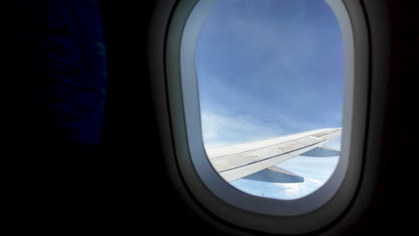 view of an airplane wing soaring through a blue sky with white clouds, as seen from the passenger window