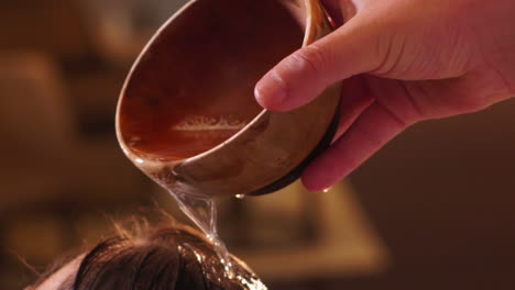 A-man´s-hand-applying-shampoo-mixture-on-a-woman´s-hair-with-a-wooden-cup