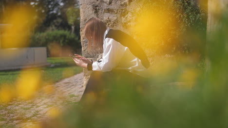 Frau-Mit-Smartphone-Im-Grünen-Park-Mit-Blühenden-Blumen