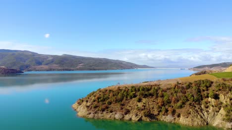 Luftaufnahme-Des-Ruhigen,-Klaren-Wassers-Des-Bergsees,-Der-Den-Blauen-Himmel-Und-Gefrorene-Weiße-Wolken-An-Einem-Sonnigen-Wintertag-Widerspiegelt