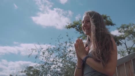 smiling pretty white woman with hands folded in namaste yoga pose, practicing gratitude in forest