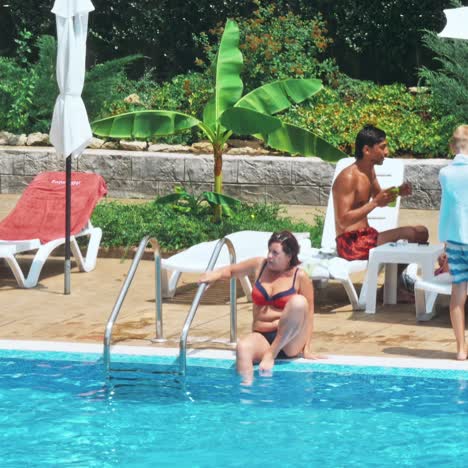 personas sentadas a la orilla de la piscina de un resort durante las vacaciones de verano