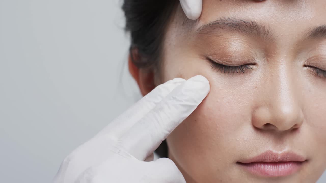 회색 배경에 있는 아시아 여성의 얼굴을 만지는 장갑을 입은 손, 슬로우 모션