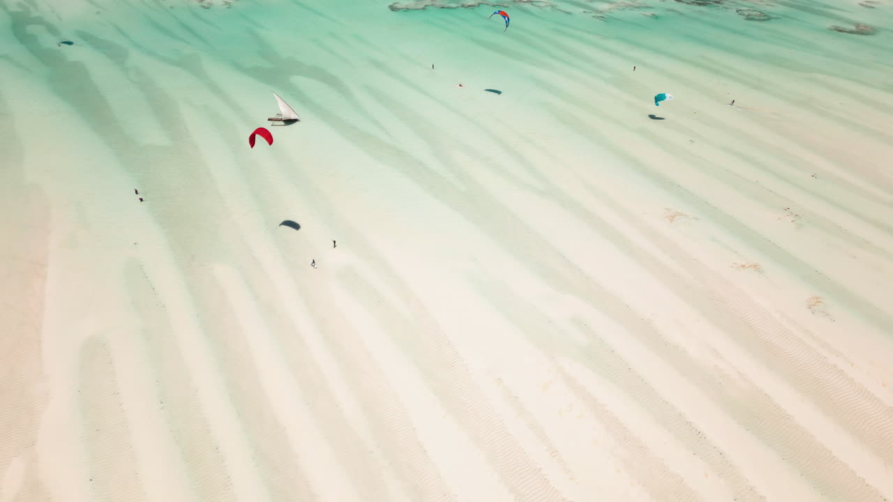 Drone shot of kitesurfers gliding over shallow waters
