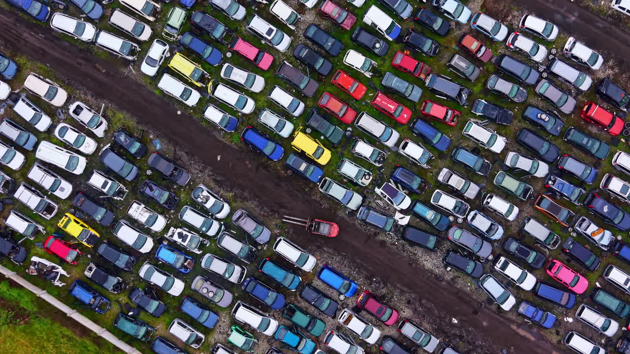 Numerose auto parcheggiate fittamente in uno sfasciacarrozze durante il giorno, che mostrano vari colori e modelli.