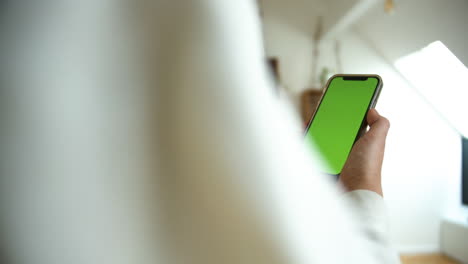 side view of a causal dressed man holding smartphone with green screen chroma key in white home background