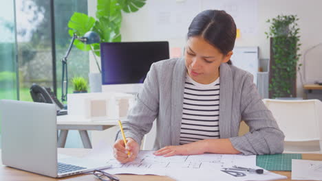 female architect in office at desk working on plans for new building