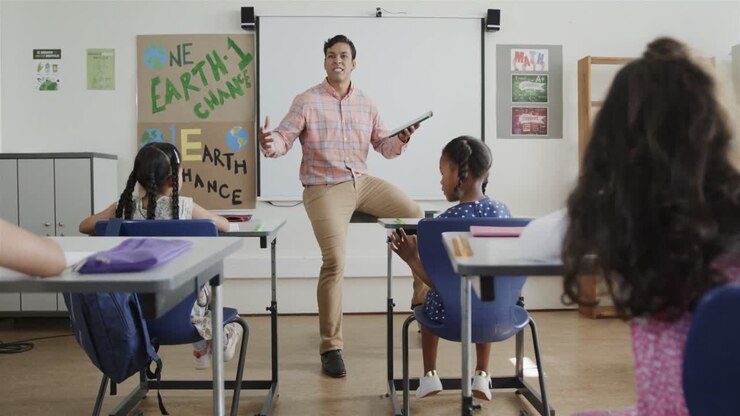 Biracial male teacher teaching diverse students in classroom at elementary school