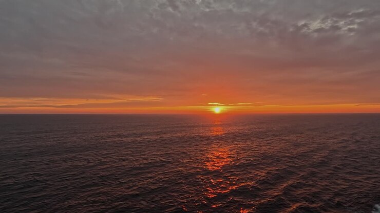 Saturated golden orange sun sets into ocean horizon from ship deck