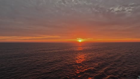 saturated golden orange sun sets into ocean horizon from ship deck