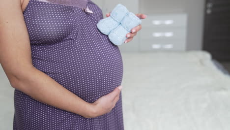 white pregnant woman in a nightgown holding little baby socks with one hand on her belly. she steps with little socks by her stomach. slow motion.