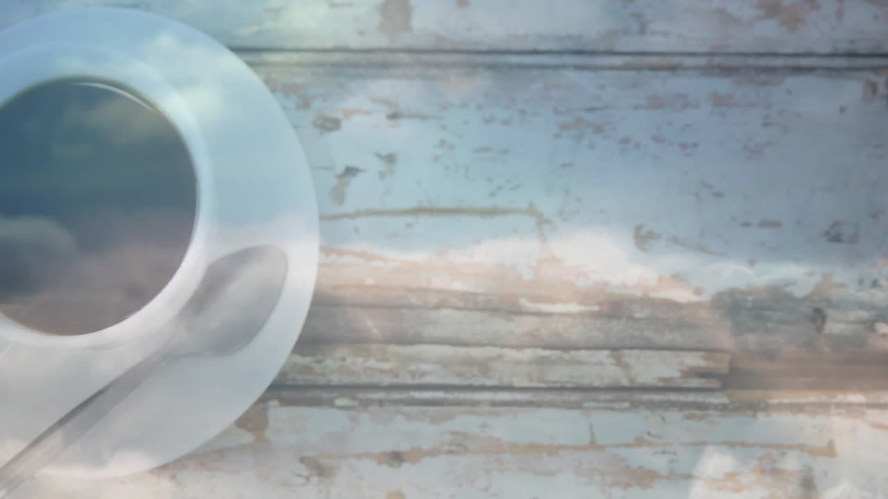 Showing white ceramic coffee cup resting on saucer with metal teaspoon on rustic wooden table