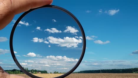 visual effect of the polarizing filter on the example of a summer rural landscape with beautiful clouds. the hand holds a circular filter, applying the polarization effect.