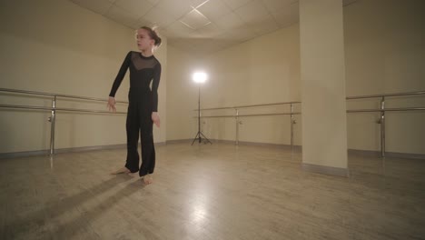 a group of young ballet students in black dancewear practicing positions in a spacious ballet studio with wooden flooring and wall-mounted barres. focused expressions and synchronized movements.