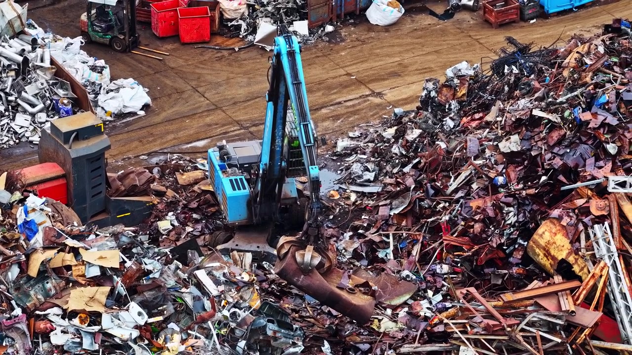 Escavatore che smista grandi cumuli di rottami metallici in un impianto di riciclaggio all'aperto