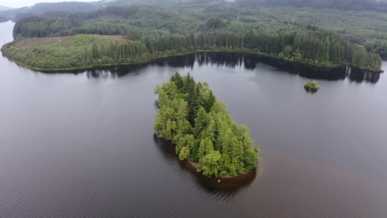 vista aérea de una pequeña isla cubierta de árboles en medio de un lago escocés en un día nublado