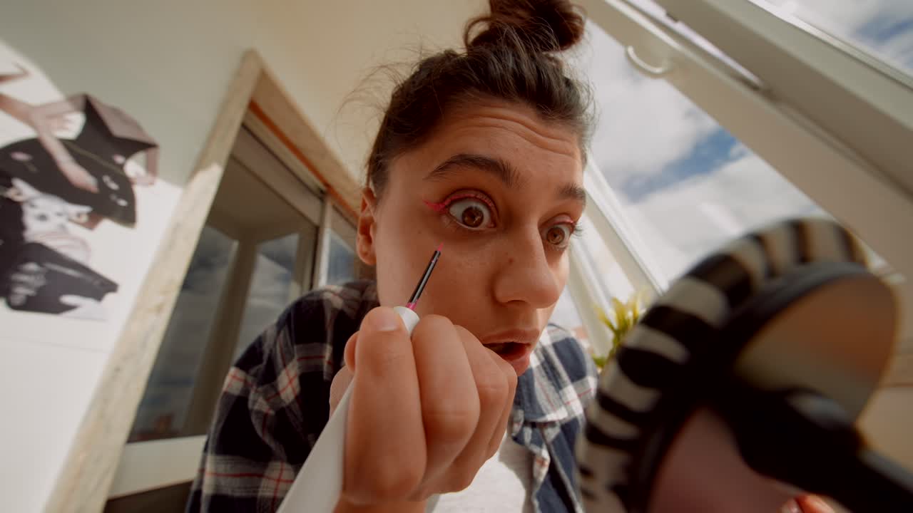 Giovane donna che applica eyeliner rosa mentre si guarda allo specchio.