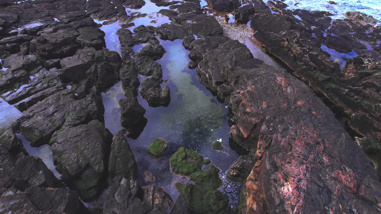 dron volando sobre la costa rocosa con el reflejo del cielo azul en bahia bustamante