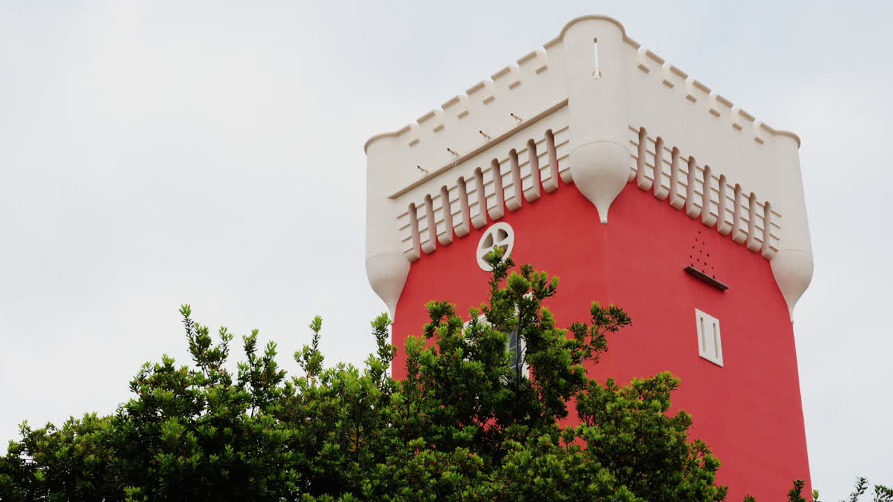 Green tree moving in the wind near the red tower of the Cremat Castle Winery over blue sky