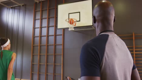 diverse female basketball player and male coach practicing shooting with ball