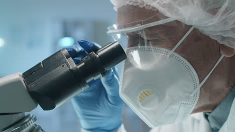 médico anciano en uniforme de protección usando el microscopio